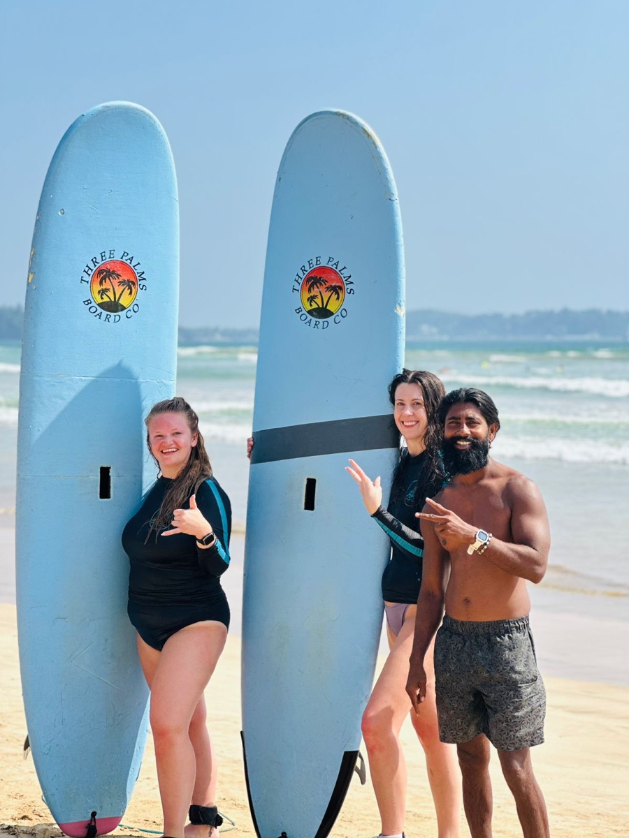 Two beginner surfers smiling with Lahiru and their surfboards